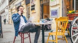 Man tourist sitting outside of a cafe with a tablet while talking on his phone