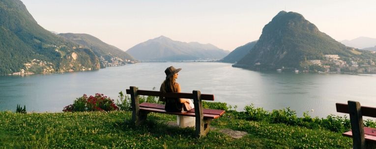 Allianz - Woman relaxes above lake and mountains on bench